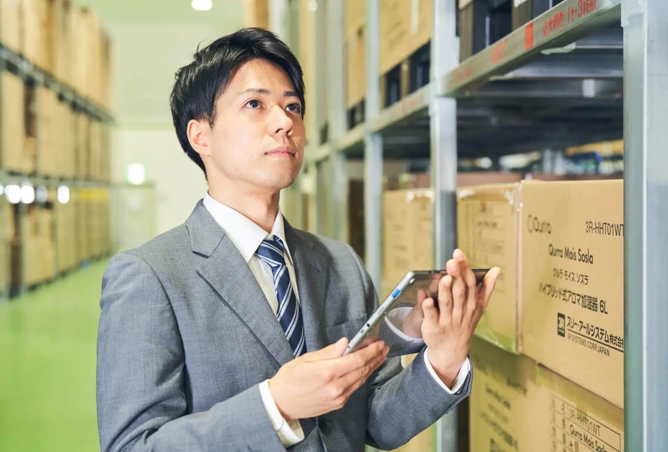 倉庫で商品の在庫確認を行う男性スタッフの写真。丁寧なコンシェルジュ型物流サポートを表現。